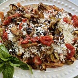 Casarecce alla norma on white platter with basil sprig garnish with spicy oil in background.