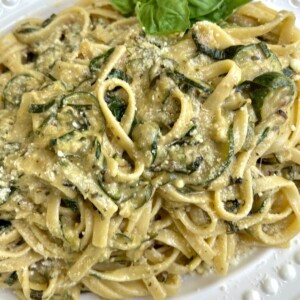 Plated creamy zucchini pasta on decorative white platter with basil garnish.