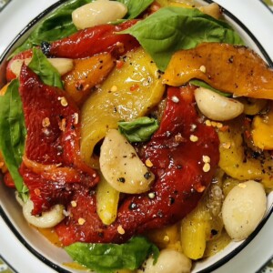 Close up of colorful Italian roasted peppers in white bowl on white plate on decorative green towel.