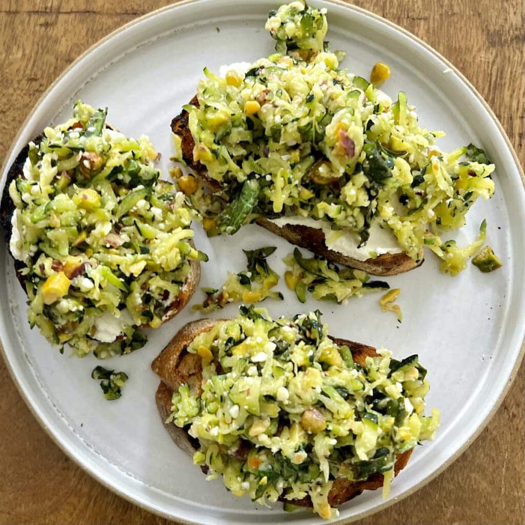 Three pieces of bruschetta topped with pesto di zucchini on a white plate.
