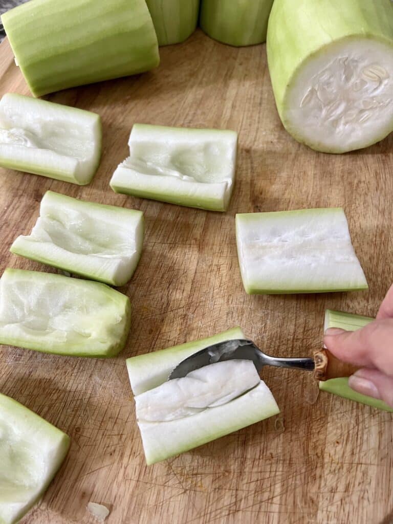 Using a grapefruit spoon to hollow out the pieces of cucuzza and also remove the seeds.