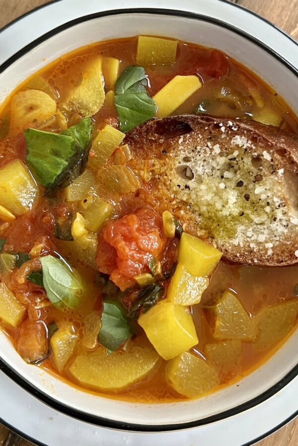 Cucuzza squash soup in white bowl with toasted and seasoned bread garnish.