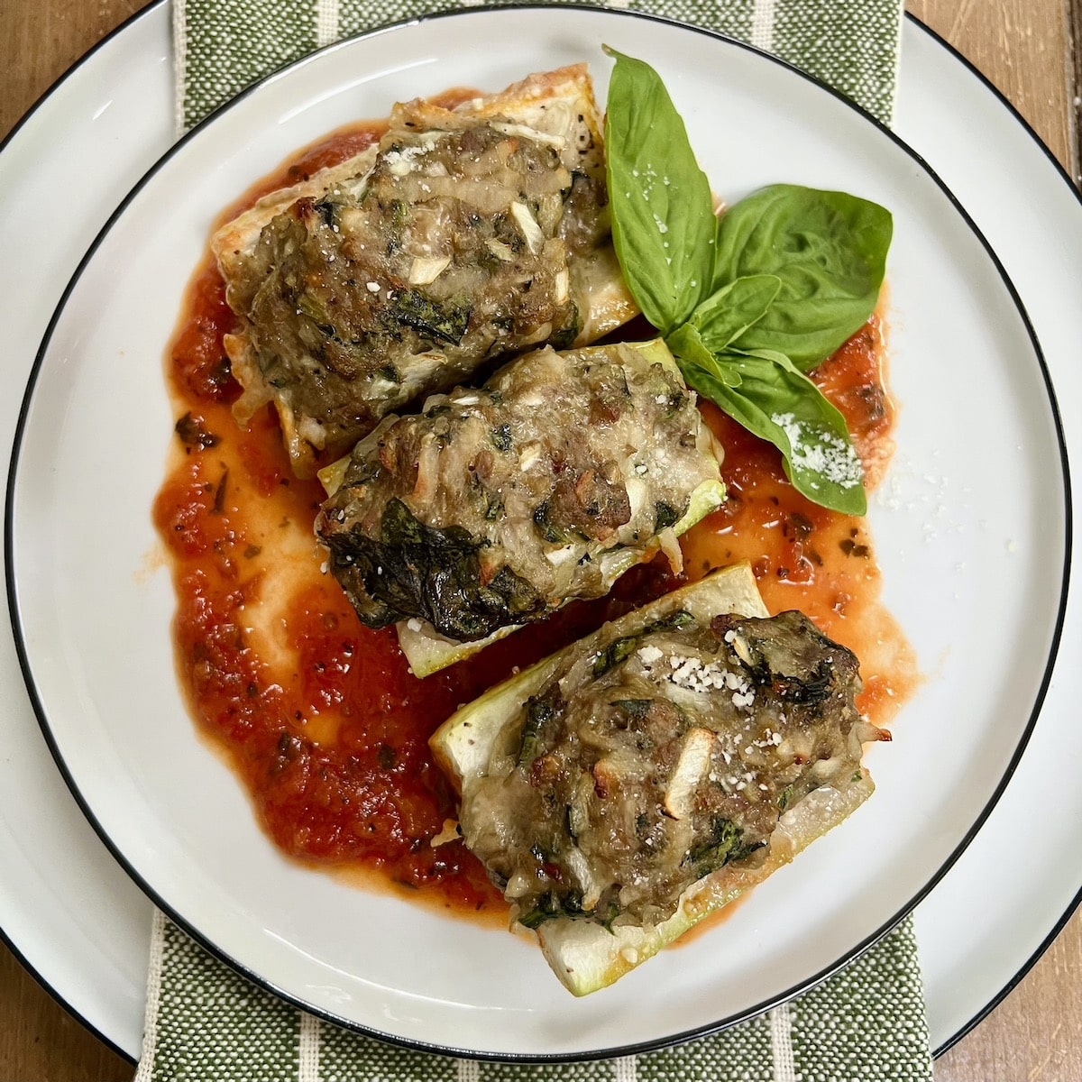 Three pieces of Baked Stuffed Cucuzza Squash over tomato sauce on white plate with basil sprig garnish.