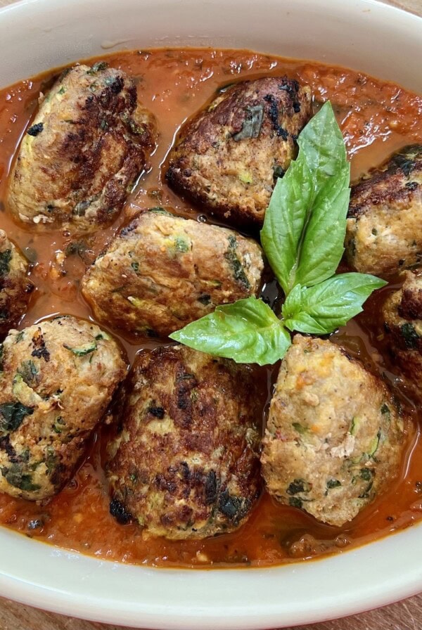 Turkey Meatballs with zucchini in tomato sauce in red baking dish with basil garnish.