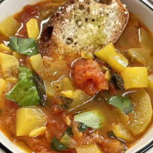 Cucuzza squash soup in white bowl with toasted and seasoned bread garnish.
