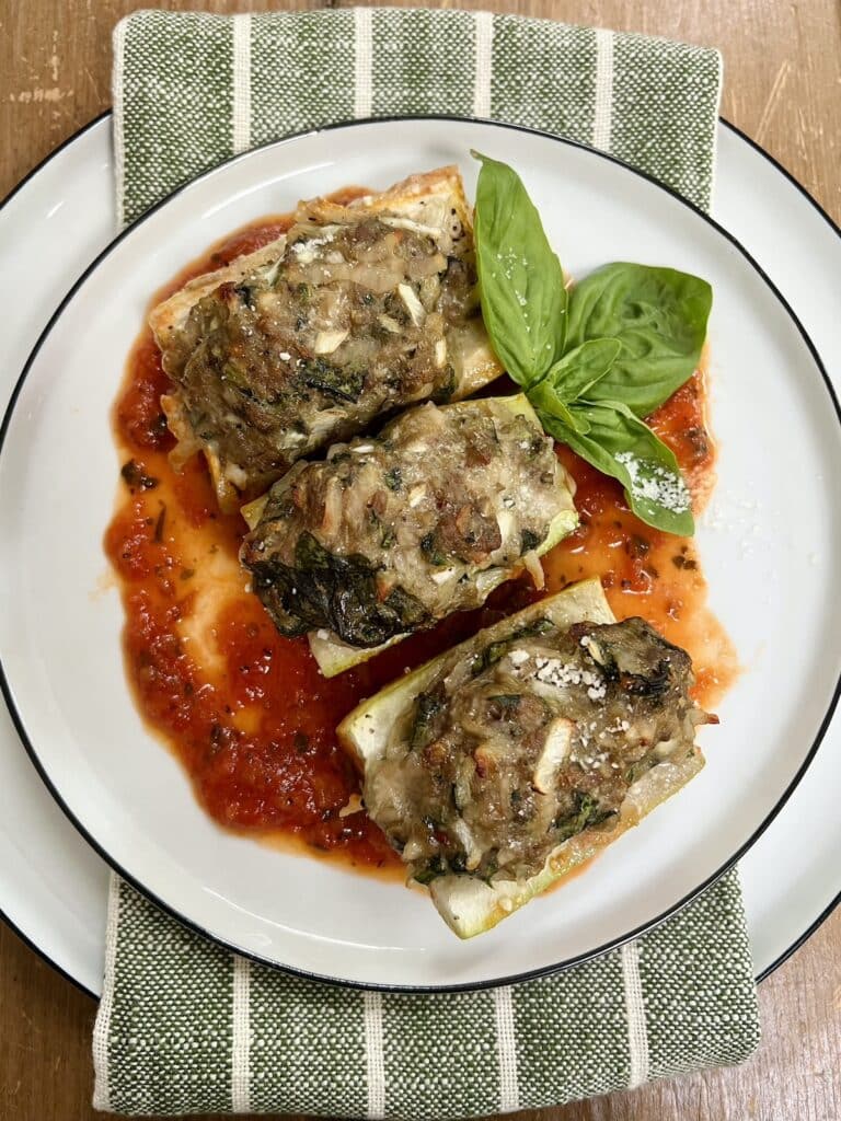 Three pieces of Baked Stuffed Cucuzza Squash over tomato sauce on white plate with basil sprig garnish.