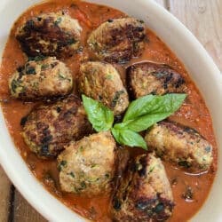 Turkey Meatballs with zucchini in tomato sauce in red baking dish with basil garnish.