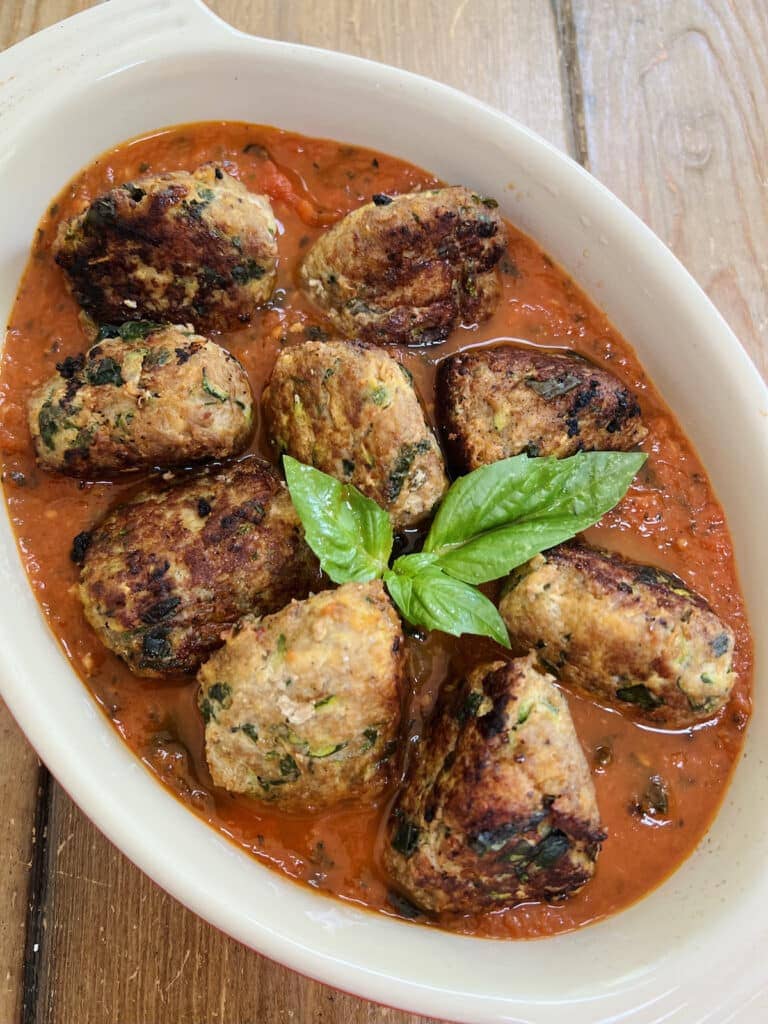 Turkey Meatballs with zucchini in tomato sauce in red baking dish with basil garnish.