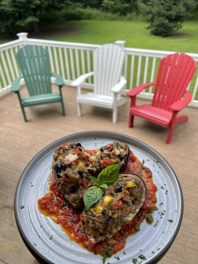 Italian Stuffed Eggplant over a bed of tomato sauce on dinner plate with fresh basil garnish with deck chairs in background.