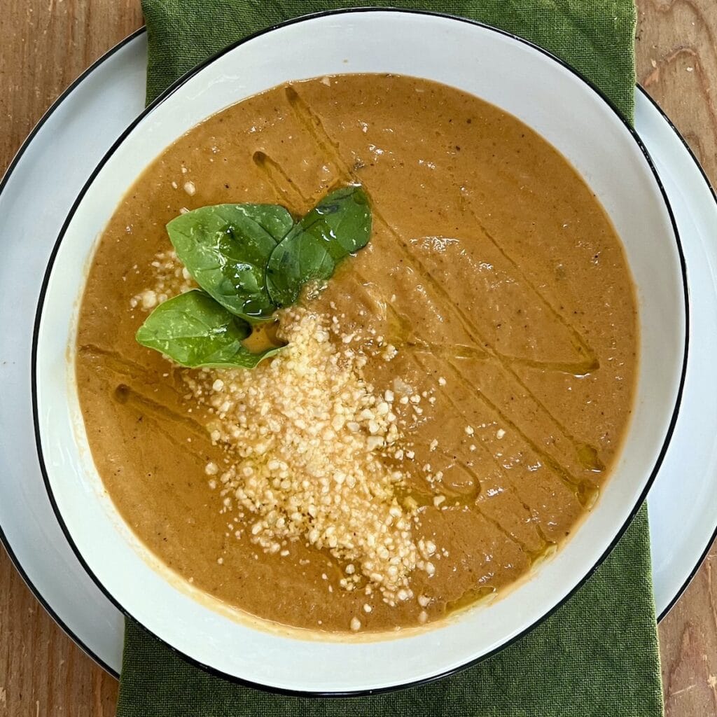Creamy eggplant soup in soup bowl with basil garnish.