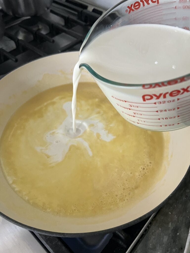 Adding cold milk to roux in pan.