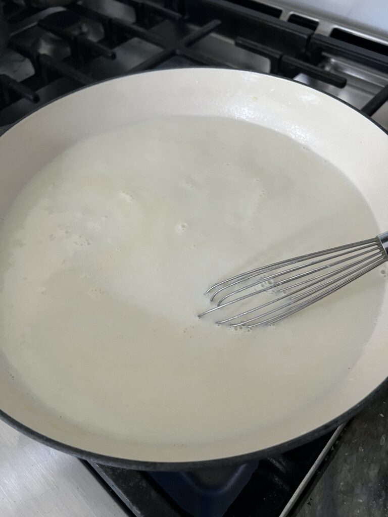 Whisking milk and roux together to make bechamel white sauce base for cheese sauce.