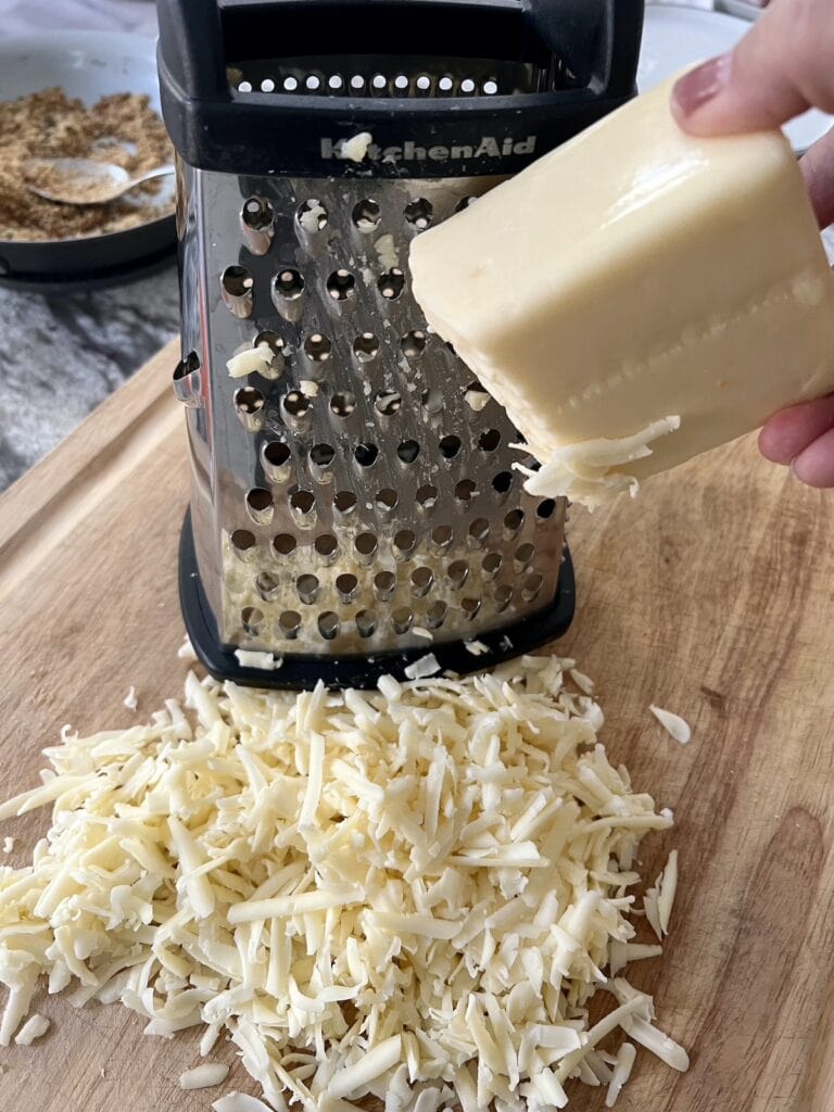 Shredding cheddar cheese on box grater.