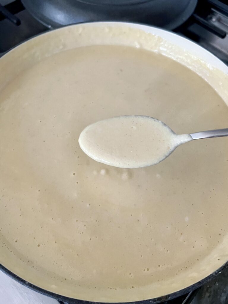 Spoonful of cheese sauce (aka mornay sauce) over potful of it.