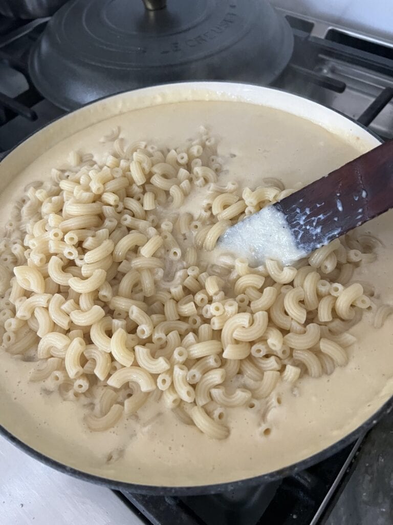Stirring cooked elbow pasta into cheese sauce with wooden utensil.