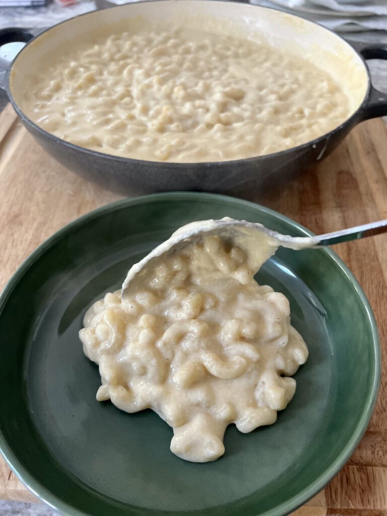 Transferring white cheddar macaroni and cheese from braiser pan to green bowl with spoon.