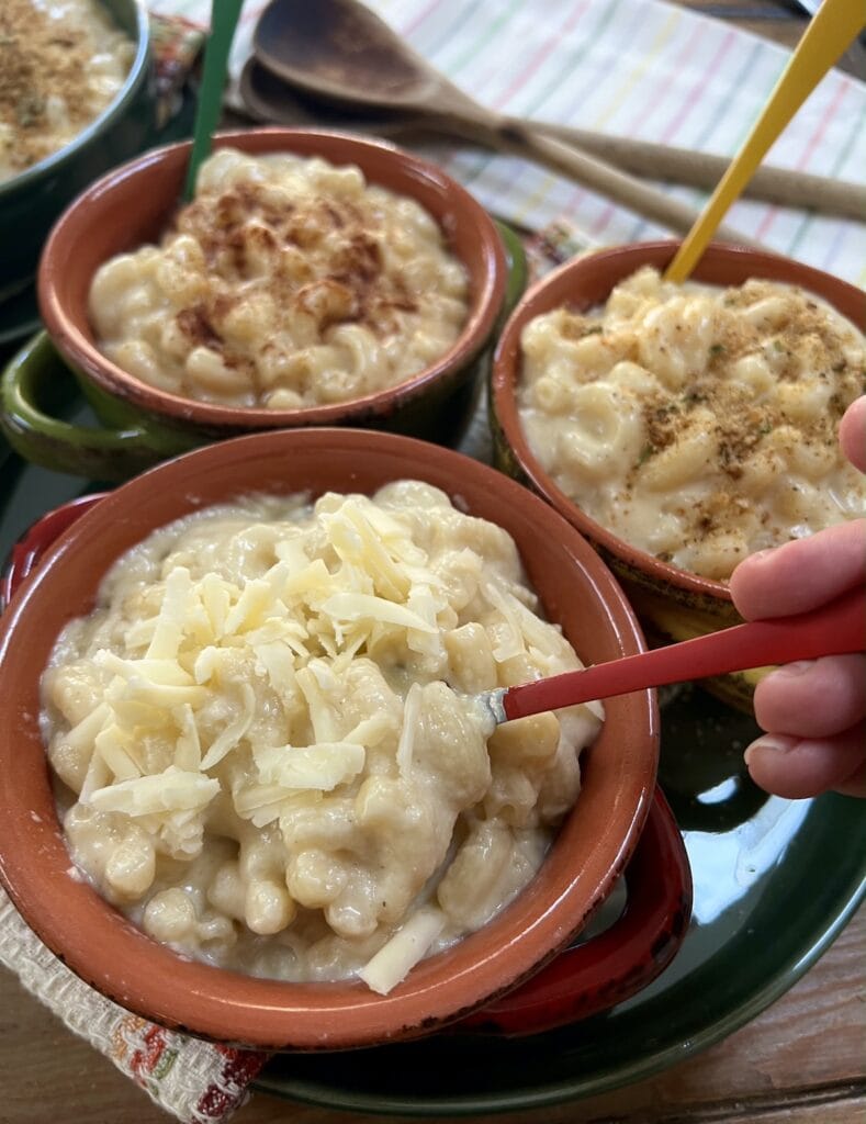 White cheddar cheese mac and cheese in 3 different colorful bowls with spoons over decorative towels.