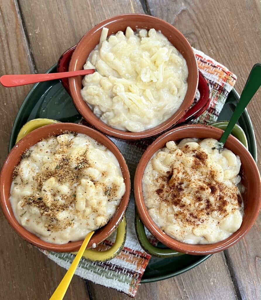 White cheddar cheese mac and cheese in 3 different colorful bowls with spoons over decorative towels.