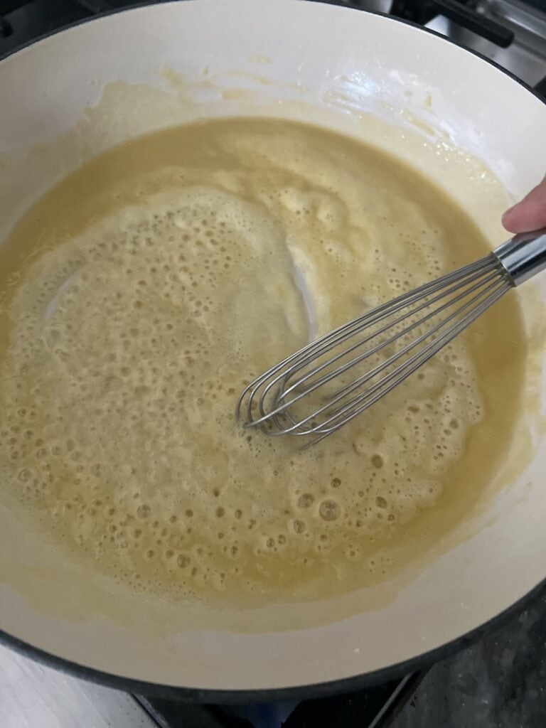 Whisking melted butter and flour together to make roux thickener.