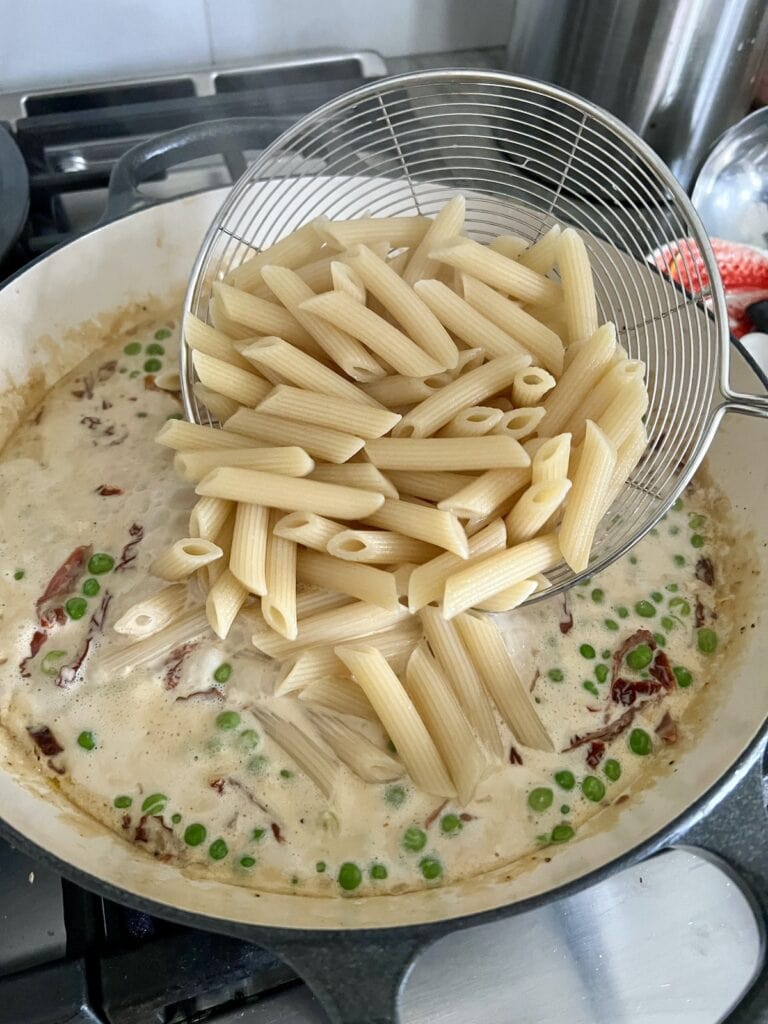Stirring in penne rigate to sauce.