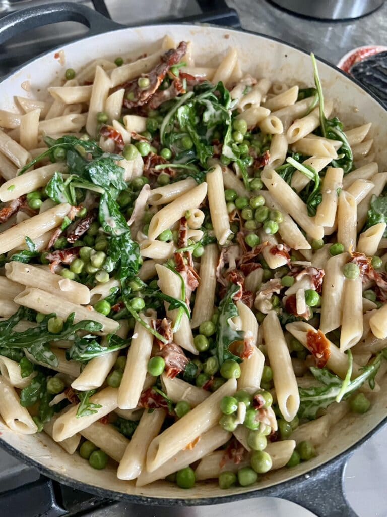 Finished pasta with prosciutto and peas in pan.