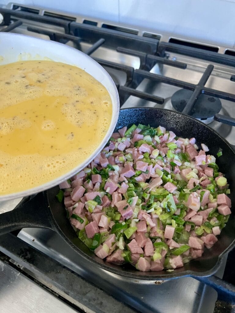 Pouring beaten eggs into the pan with ham and green onions.