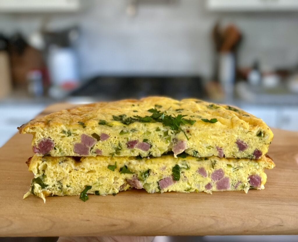 Two halves of easy ham and cheese frittata stacked on top of each other on cutting board.