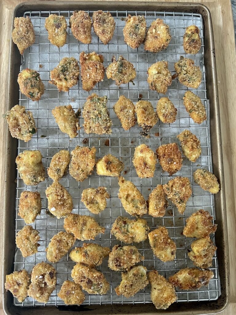 Just fried, crispy artichoke hearts on a rack over a sheet pan.
