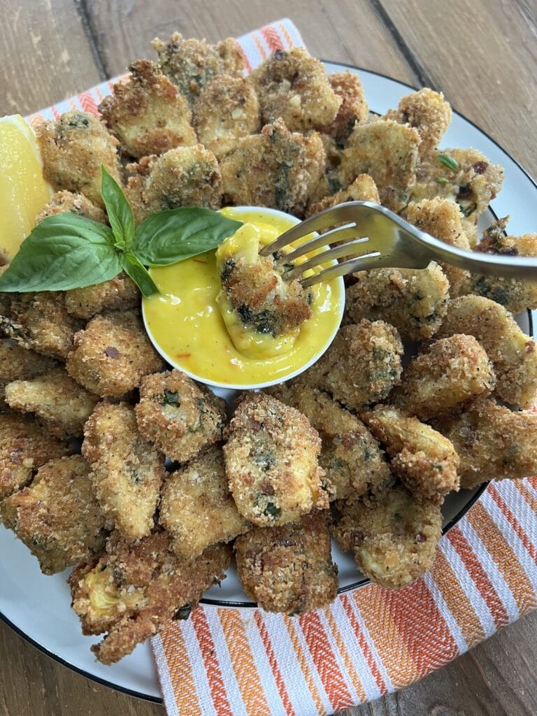 One of a plateful of crispy fried italian artichoke hearts on a fork being dipped into a saffron aioli dipping sauce.