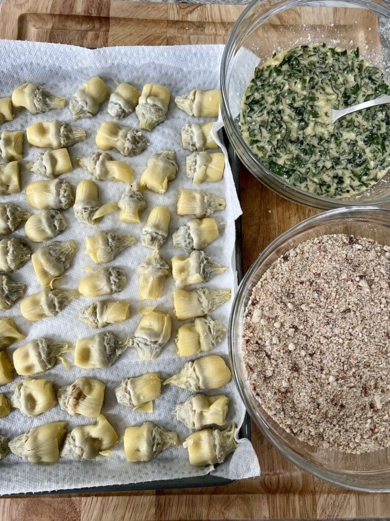 Bowls of egg mixture and seasoned breadcrumbs next to prepped and dried, halved artichoke hearts.