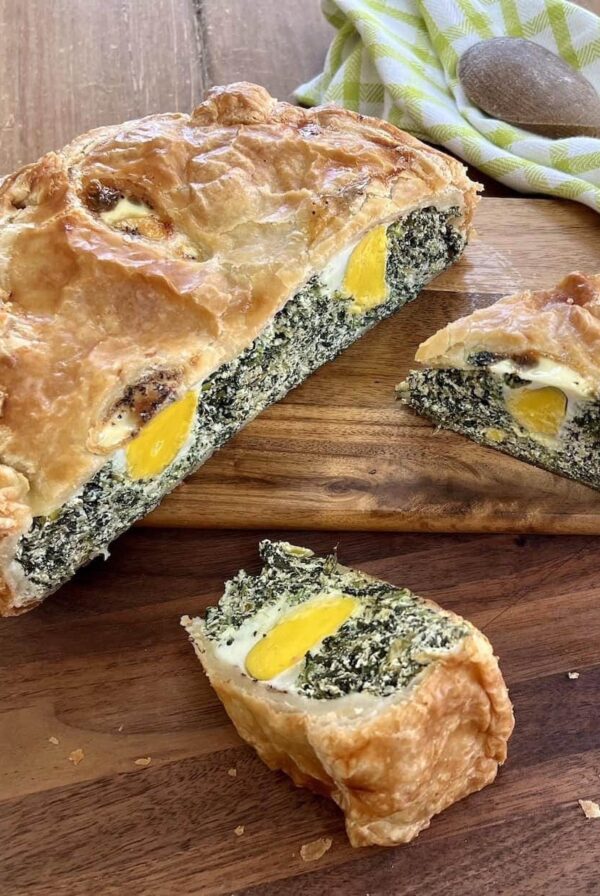 A pie with spinach and eggs on a cutting board.