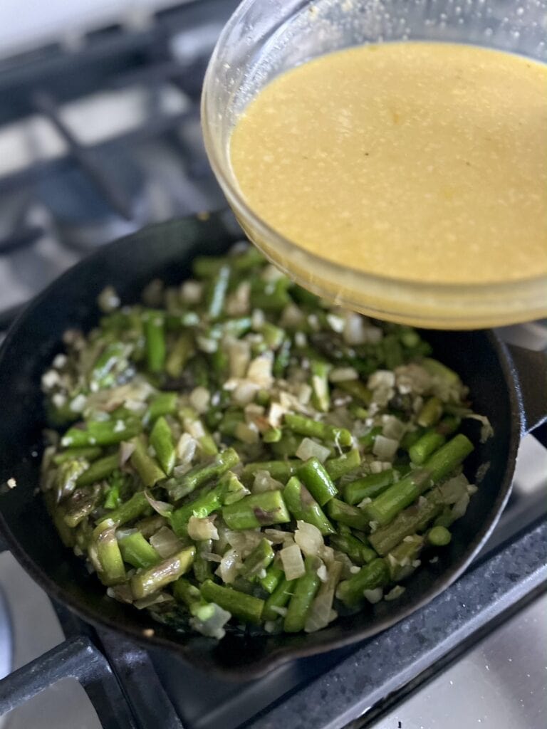 Pouring egg mixture into cast iron pan with sautéd vegetables.