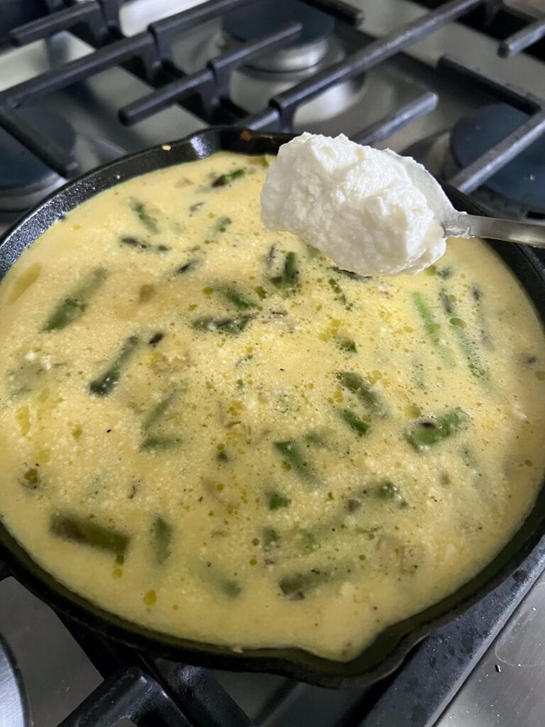 Adding a dollop of ricotta cheese to the asparagus and egg frittata mixture in pan.