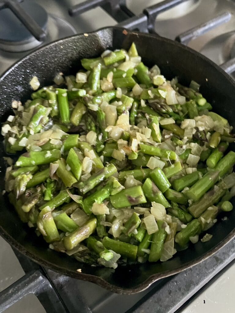 Sautéing chopped asparagus pieces and garlic with onions in cast iron pan.