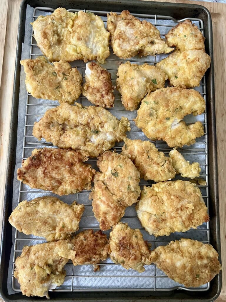 Cooked, egg and cheese-battered chicken breast draining on wire rack over sheet pam.