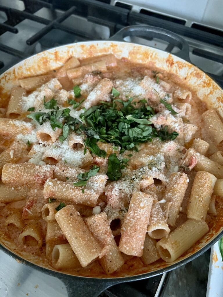 Grated cheese and chopped fresh basil added to creamy ricotta tomato pasta in pan.