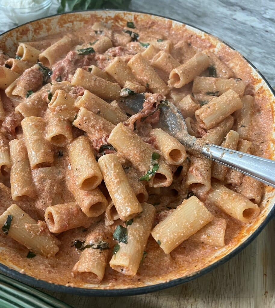 Finished creamy tomato and ricotta pasta in pan with stainless steel spoon.