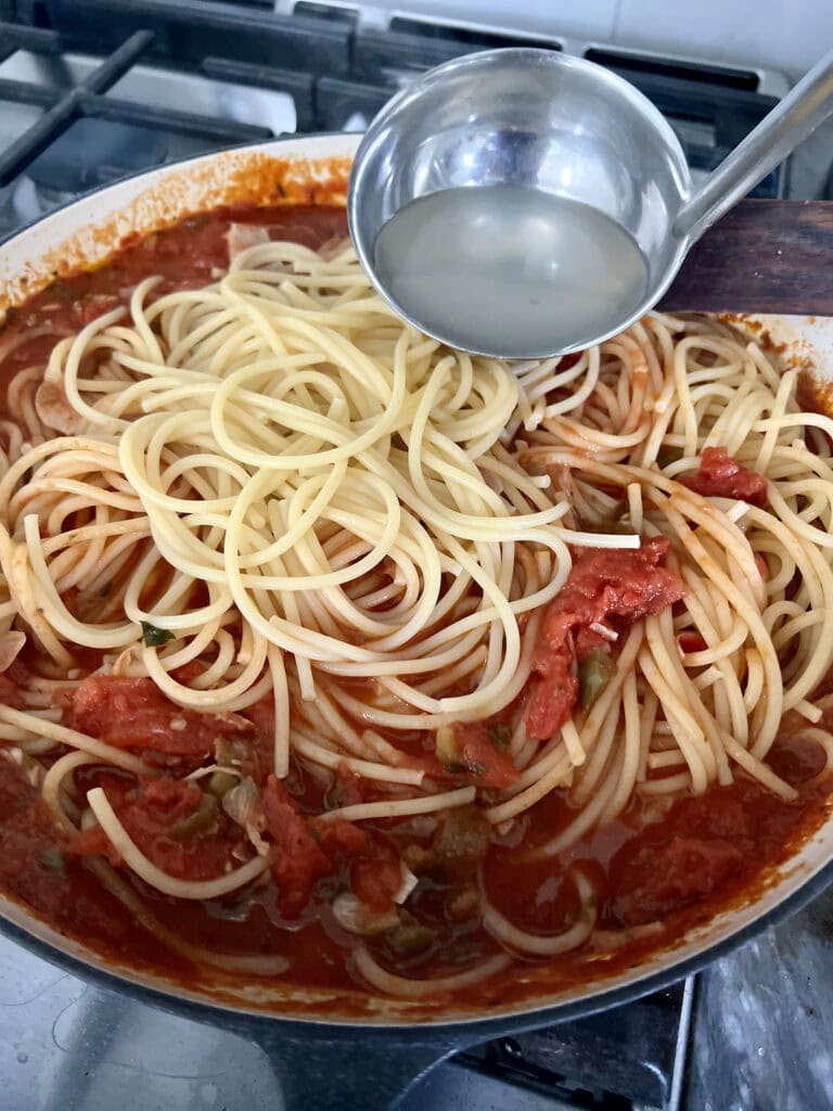 Adding pasta water to spicy shrimp pasta.