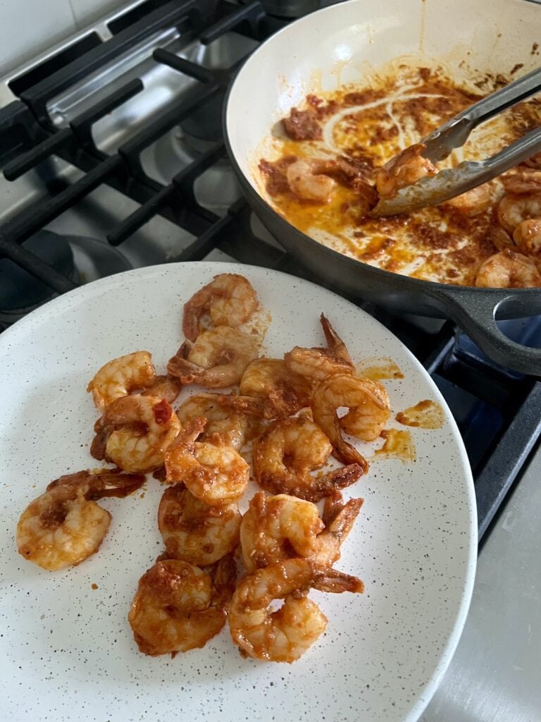 Transferring spicy tomato shrimp from pan to white plate with tongs