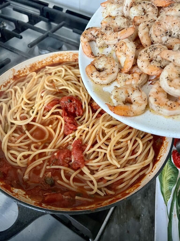 Adding the cooked shrimp back to the pasta with arrabbiata sauce.