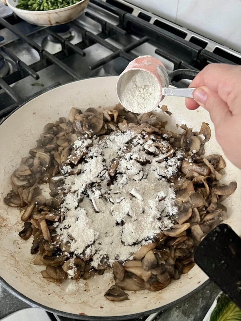 Sprinkling flour over cooked mushrooms.