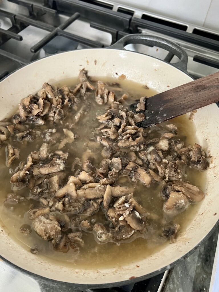 Mixing broth into mushrooms in pan.