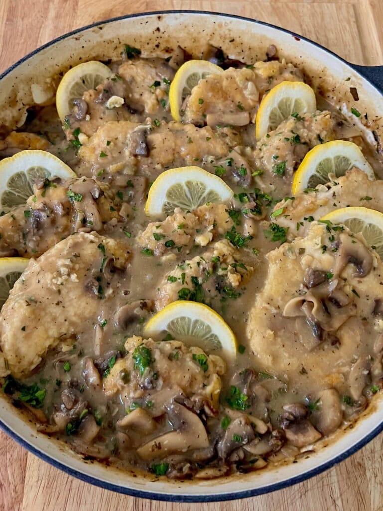 Finished Italian chicken francese with mushrooms in pan with lemon slices.