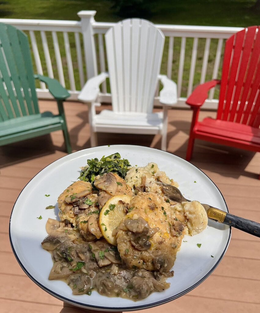 Chicken Francaise with sides on white dinner plate with deck chairs in backgound.