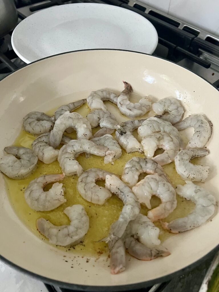 Searing shrimp on olive oil in pan.