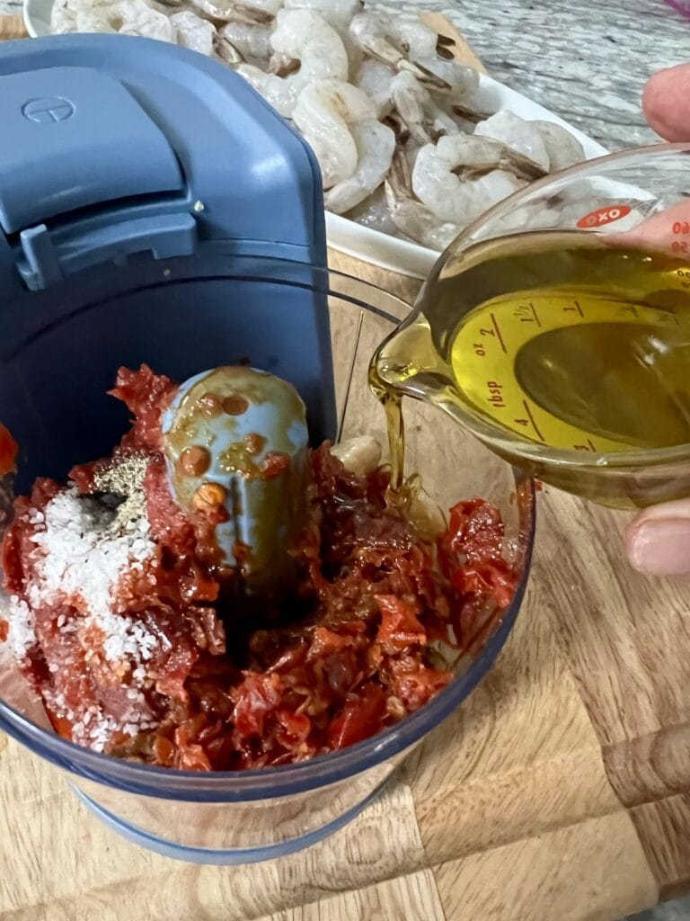 Pouring olive oil into food processor with other marinade ingredients.