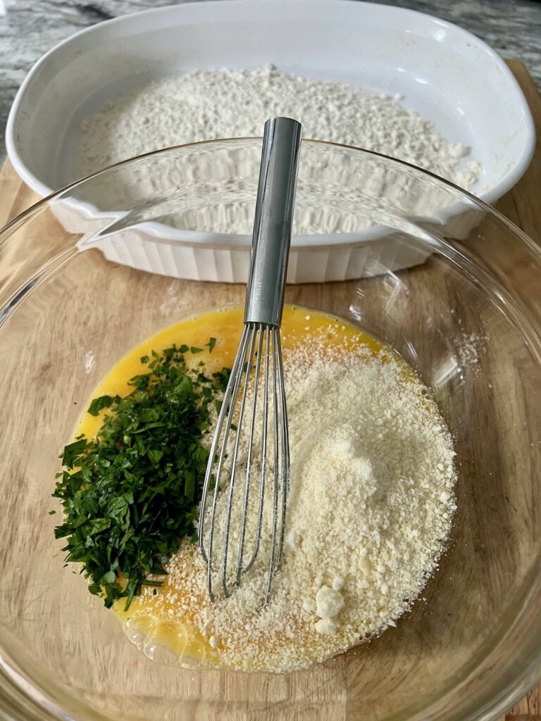 Eggs, chopped parsley and grated cheese in bowl about to be mixed together, with flour in the backgound.