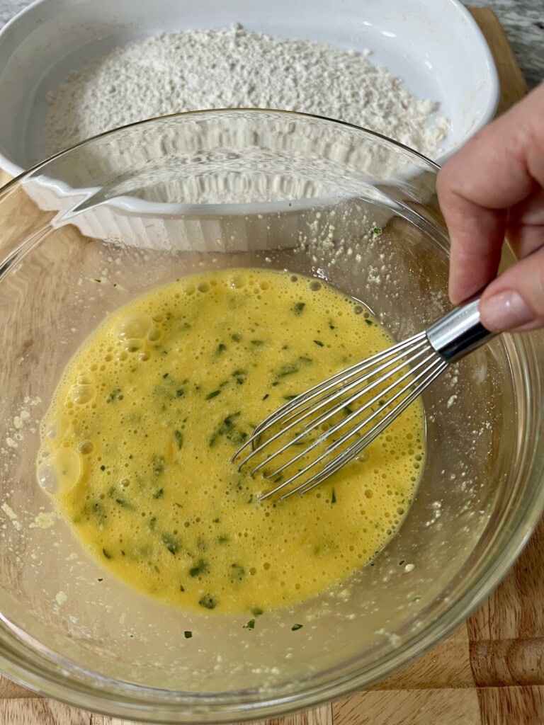Whisking eggs, chopped parsley and grated cheese together, with flour in the backgound.