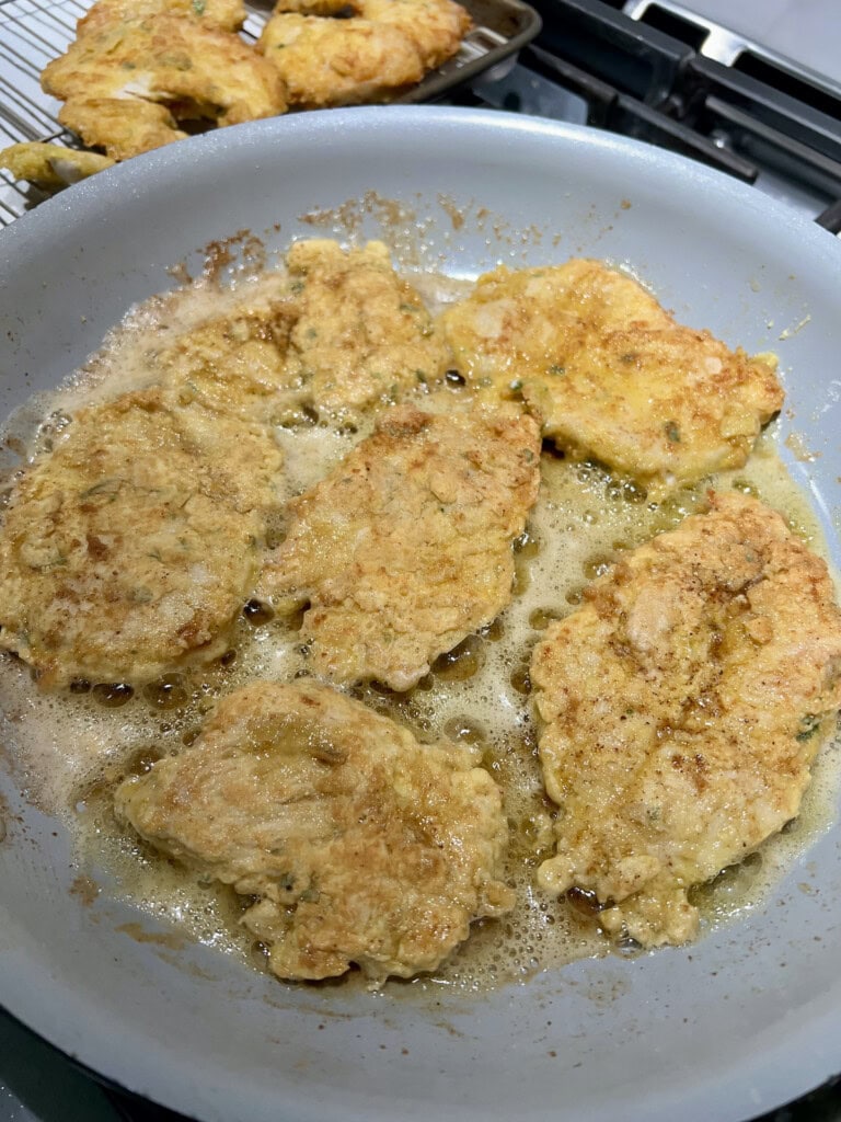 Cooking egg-battered chicken breast in oil and butter in pan.