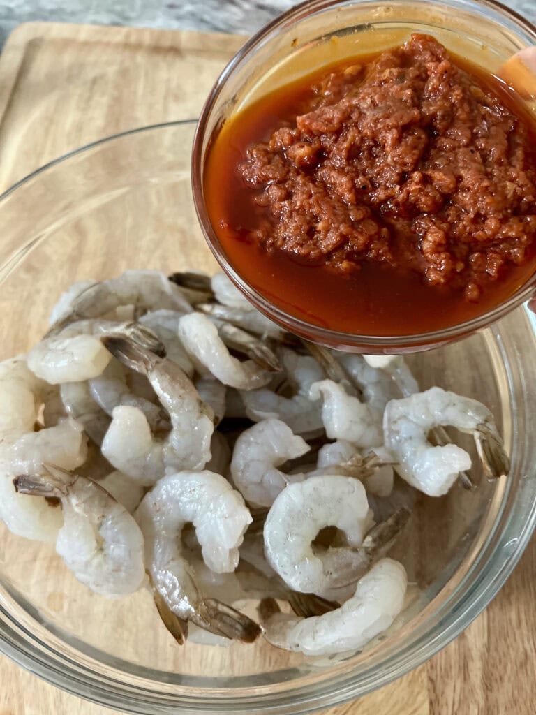 Pouring spicy tomato marinade into bowl of raw shrimp.